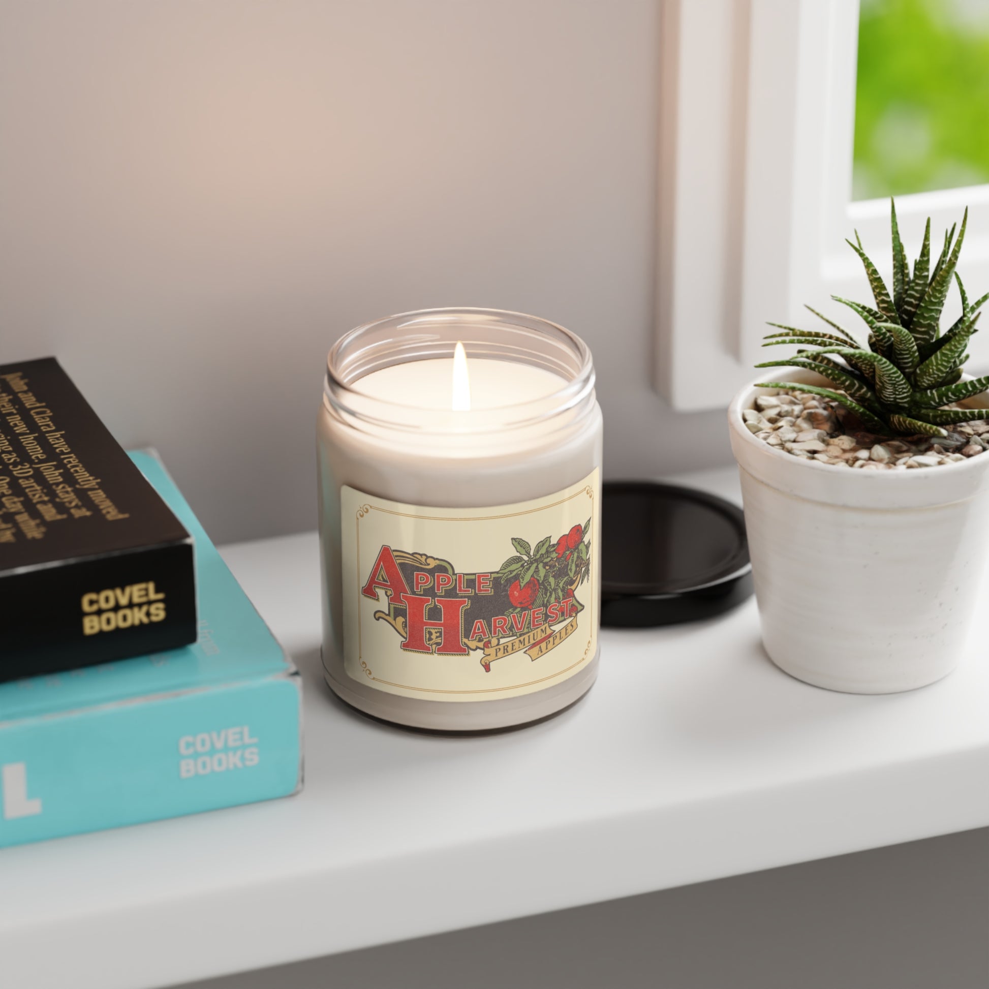 Apple Harvest lit 9 oz soy candle sitting on shelf next to books, plant and window