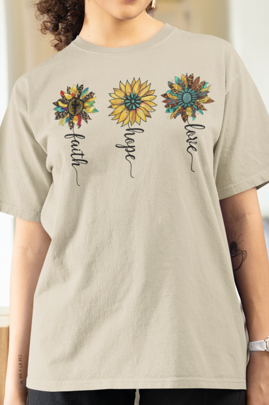 Sand colored t-shirt with 3 different rustic vintage style sunflowers each with a different word as the stem.  Words are faith, hope and love. Graphic is on front of the shirt. Modeled by Woman