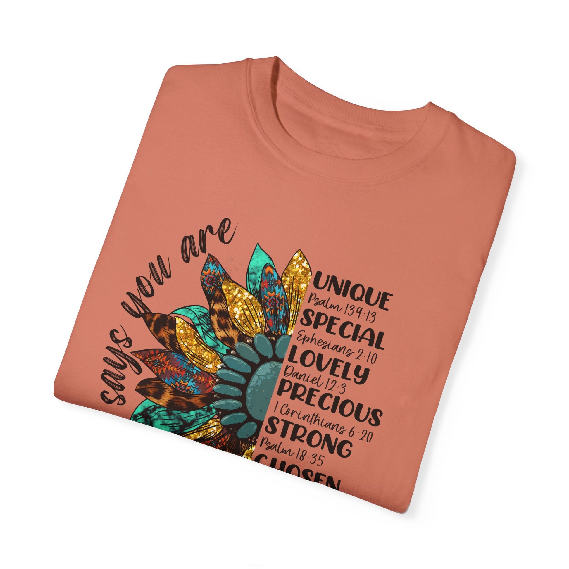 Terracotta color folded t-shirt with half a sunflower with gold, teal and leopard print petals and a teal middle with the words "God says you are" arching it on the left of the flower and the words listed with referenced bible verses "unique, special, lovely, precious, strong, chosen and forgiven" filling the the opposite side of the flower