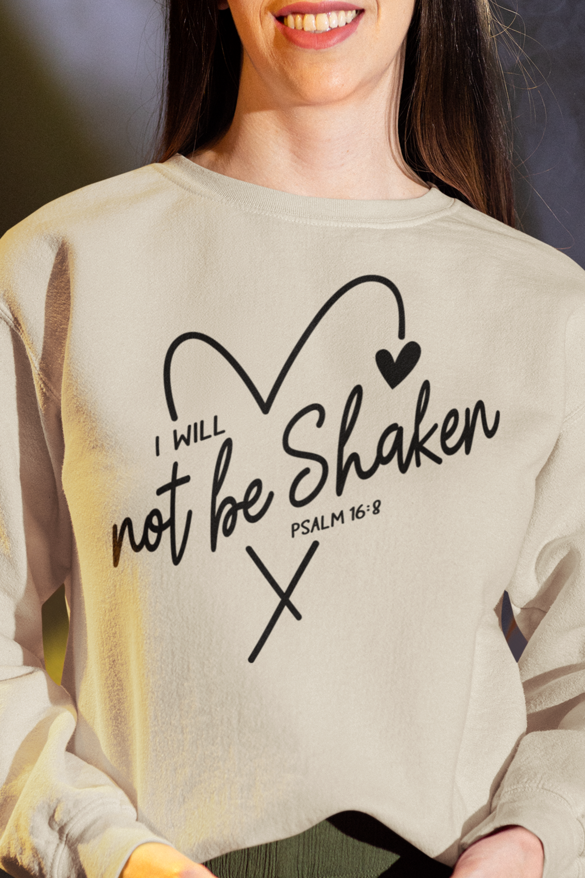 Sand Color Crewneck sweatshirt with a drawn heart and the words "I Will Not Be Shaken" Psalm 16:8 on the front, worn by woman