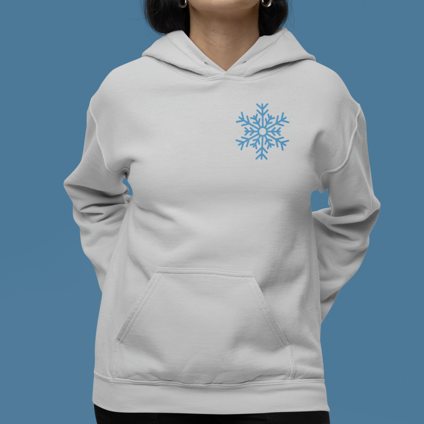 Ash colored hoodie with graphic on front and back. Front has snow flake on left pocket chest pocket area.  Back has a cute skeleton with winter hat drinking an iced coffee surrounded by the words just chill in a circle with decorative elements filling the gap between the words in a circle.  Circle also has snowflakes filling in the open space around the skeleton. Woman modeling front of shirt