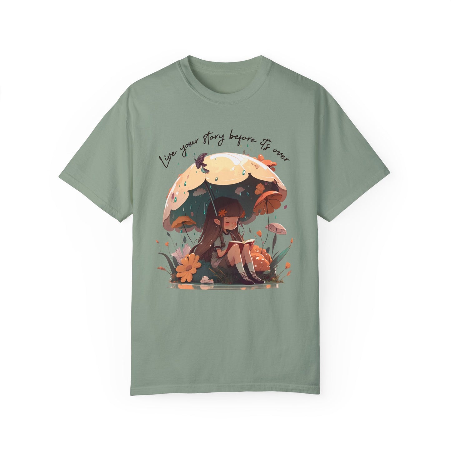 Bay colored T-Shirt with girl sitting under an umbrella reading a book in the rain surrounded by flowers and mushrooms with the words live your story before it's over arching above the umbrella