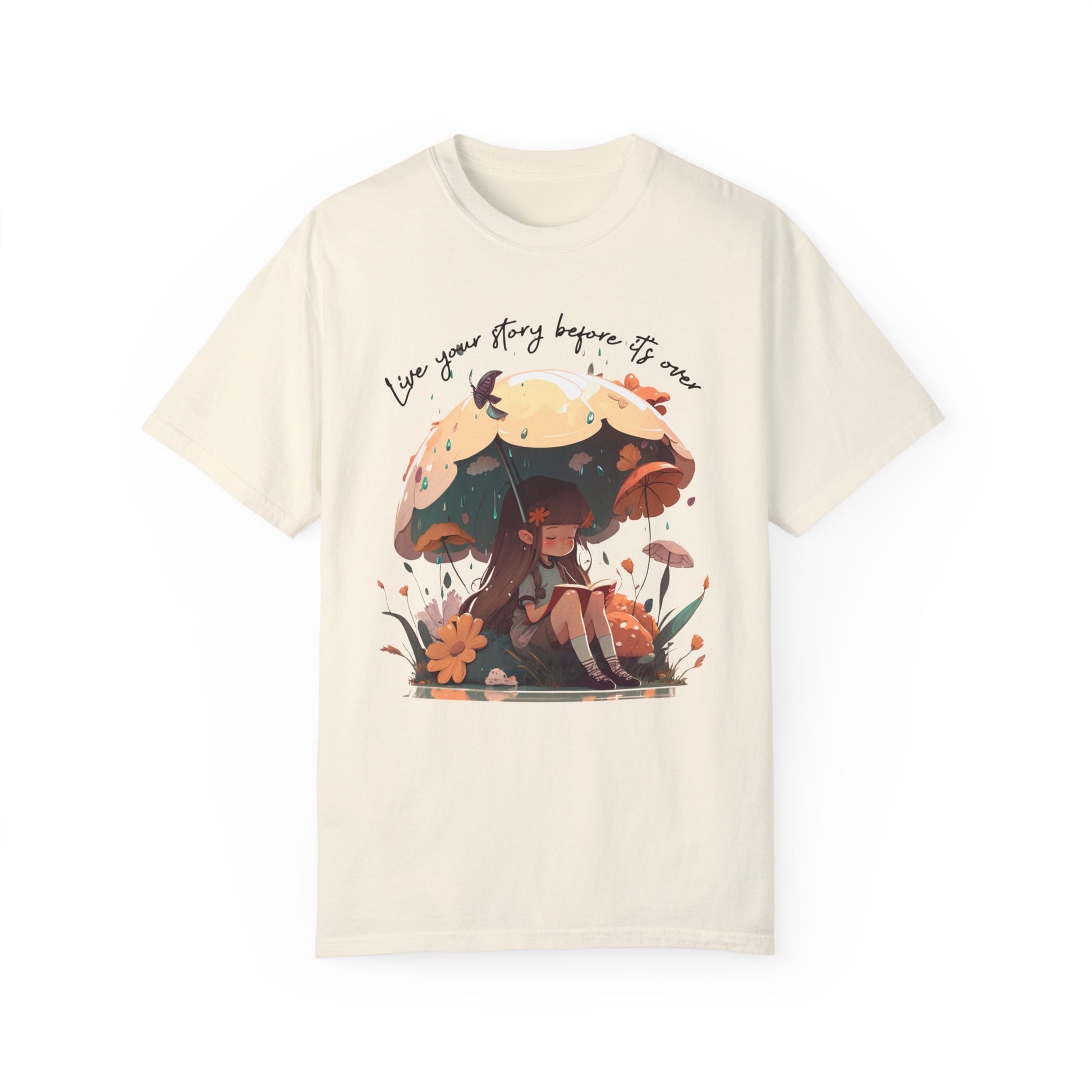 Ivory colored T-Shirt with girl sitting under an umbrella reading a book in the rain surrounded by flowers and mushrooms with the words live your story before it's over arching above the umbrella