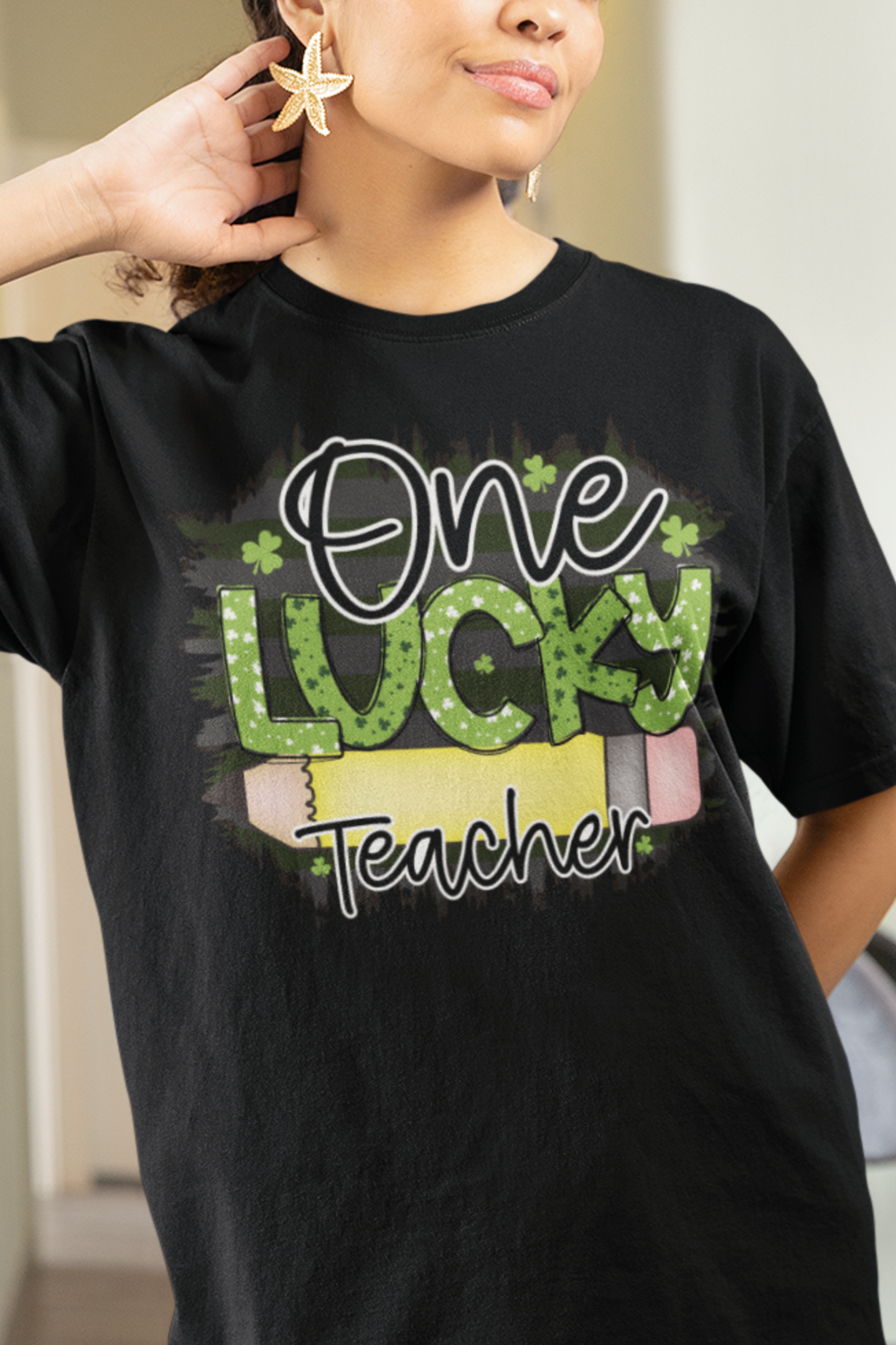 Black T-shirt with the words One in black Lucky in Green with White and Green Shamrocks and Teacher in Black with white outline.  There is a pencil graphic between the words lucky and teacher.