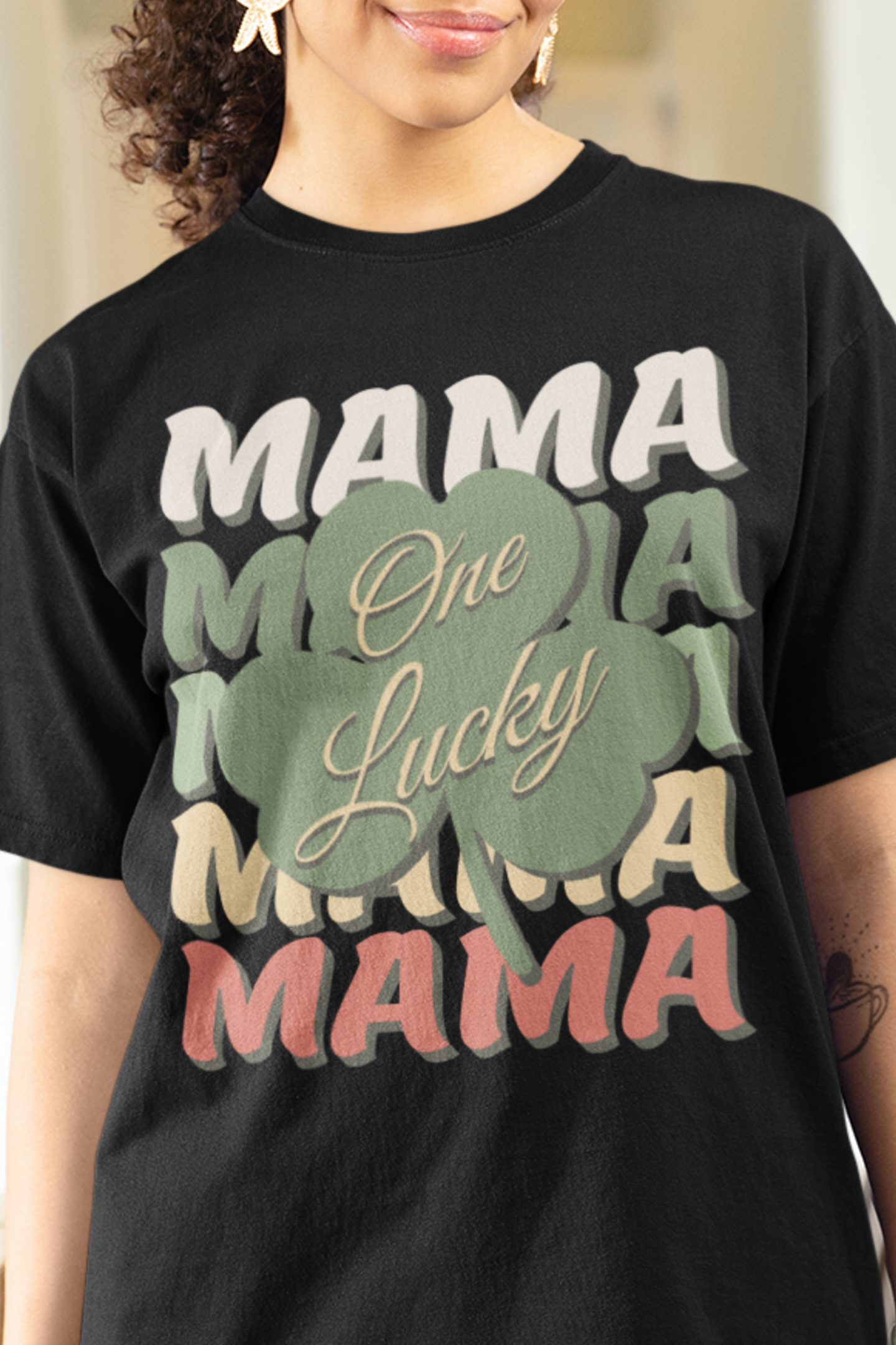 Black color t-shirt for mom with the words mama listed 5 times each in a different color with a shamrock on top and the words one lucky spanning across the shamrock for the final message of "One Lucky Mama". Woman Mock up