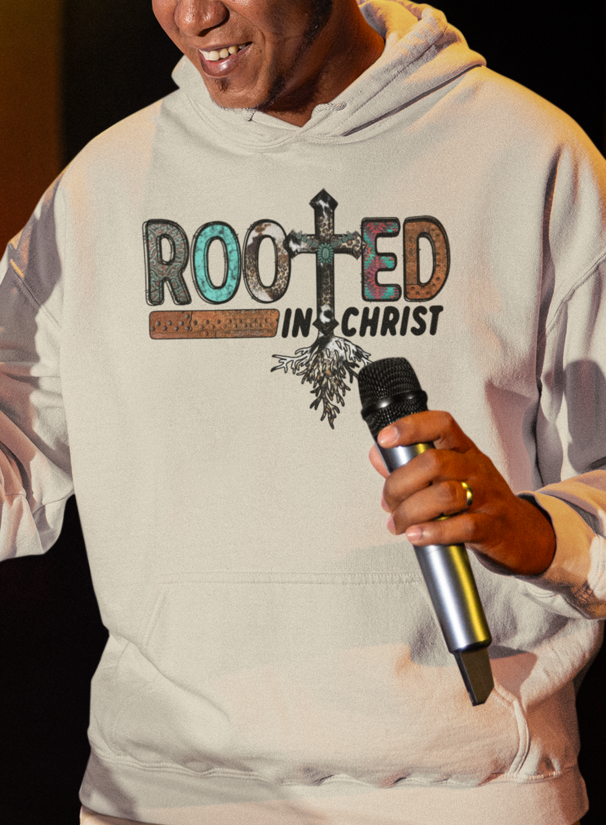 Sand colored hoodie sweatshirt with the words Rooted in Christ across the chest with roots growing out of the T in the word rooted represented by a cross