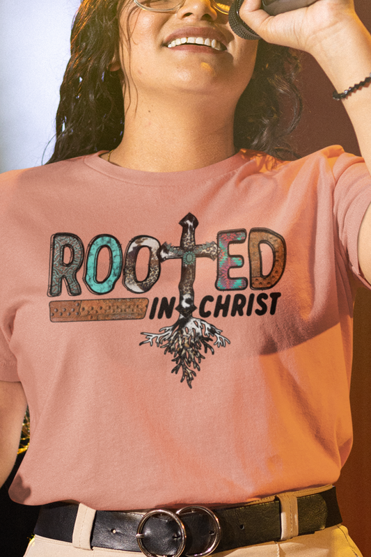 Woman wearing terracotta colored T-shirt with the words Rooted in Christ across the chest with roots growing out of the T in the word rooted represented by a cross