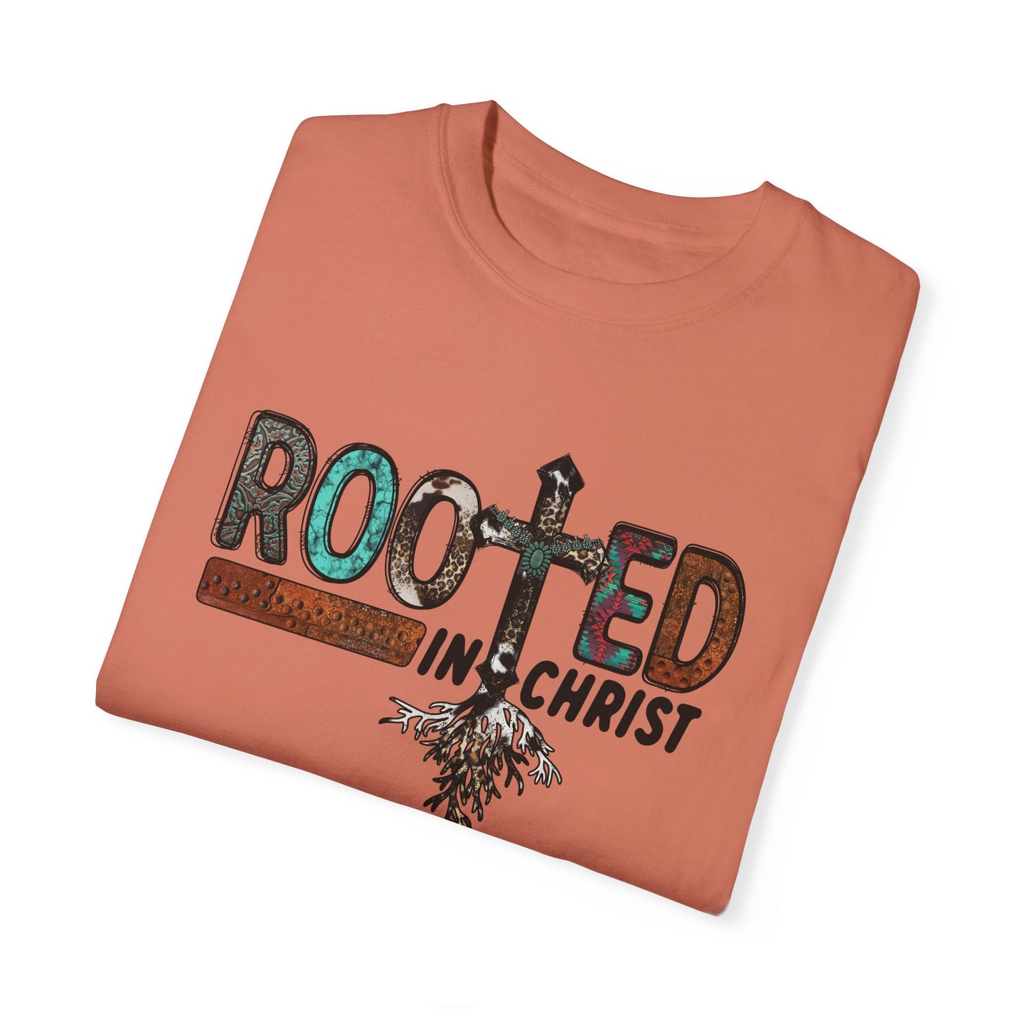 Folded terracotta colored T-shirt with the words Rooted in Christ across the chest with roots growing out of the T in the word rooted represented by a cross