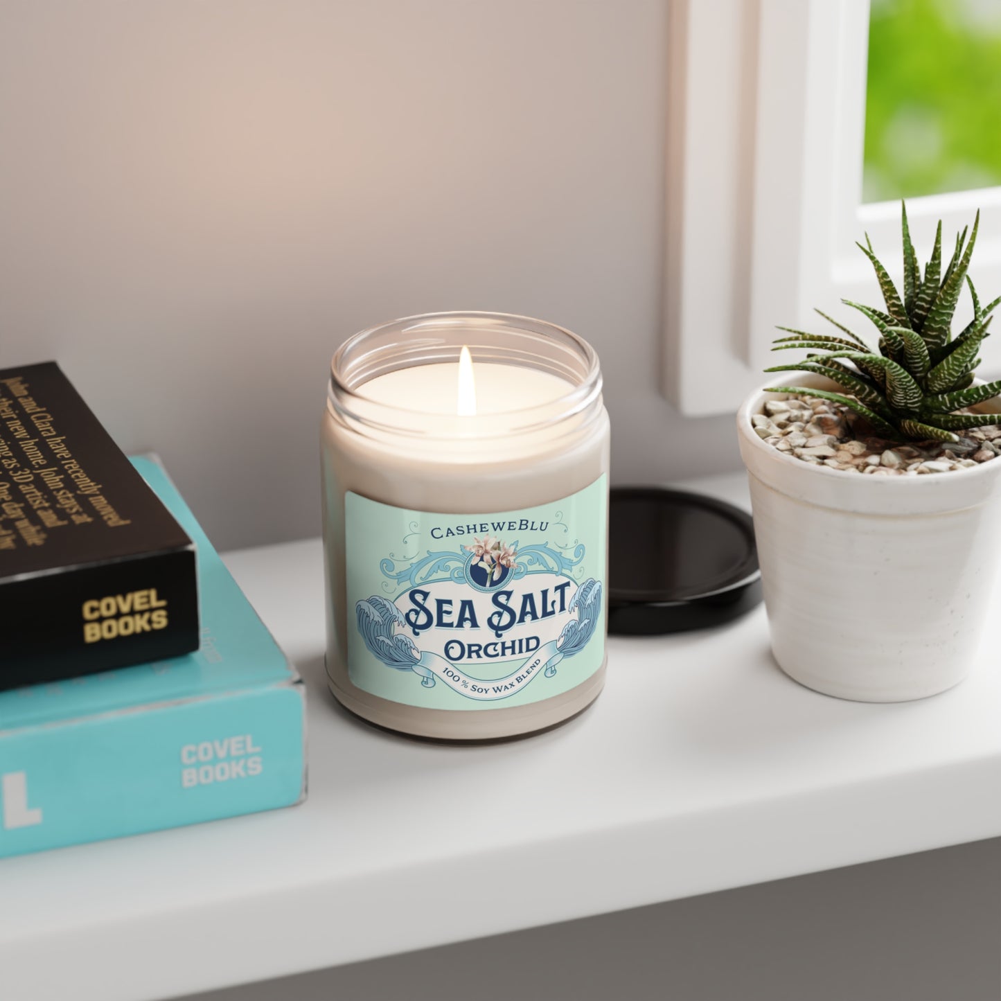 Sea Salt Orchid lit 9 oz soy candle sitting on shelf next to plant, books and window