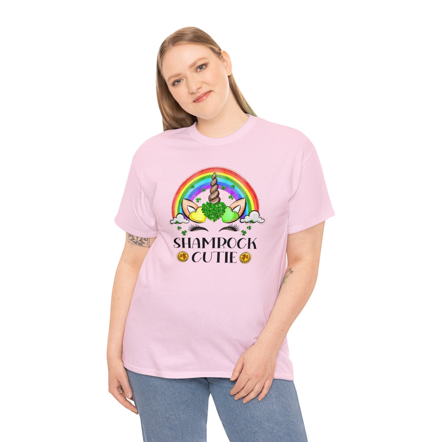 Light pink color St. Patrick's Day T-Shirt with a rainbow surrounding a unicorn with hearts at the base of the horn one made up of shamrocks and the words Shamrock Cutie under the unicorn face. Mock-up with woman model.