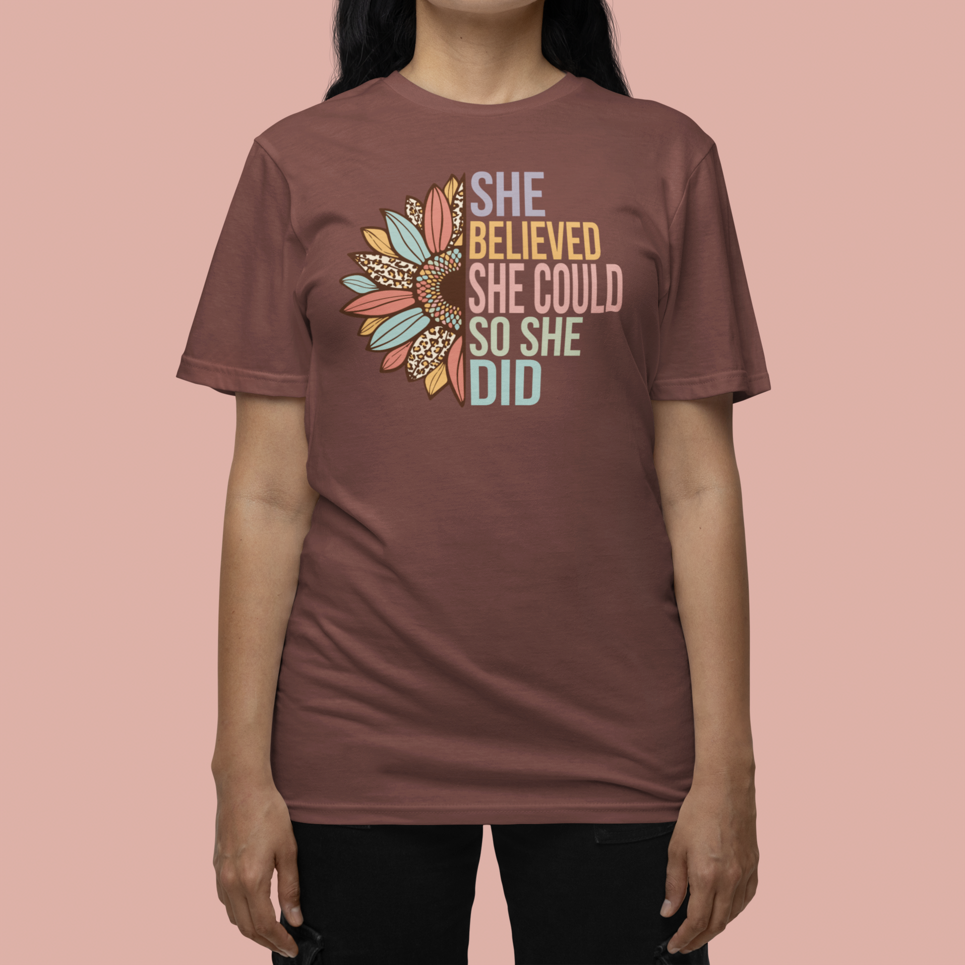 Vineyard colored t-shirt with the saying "She Believed She Could So She Did" as half of the sunflower and a retro design other half of the flower with petals of leopard print, teal, rust and golden yellow worn by a woman.