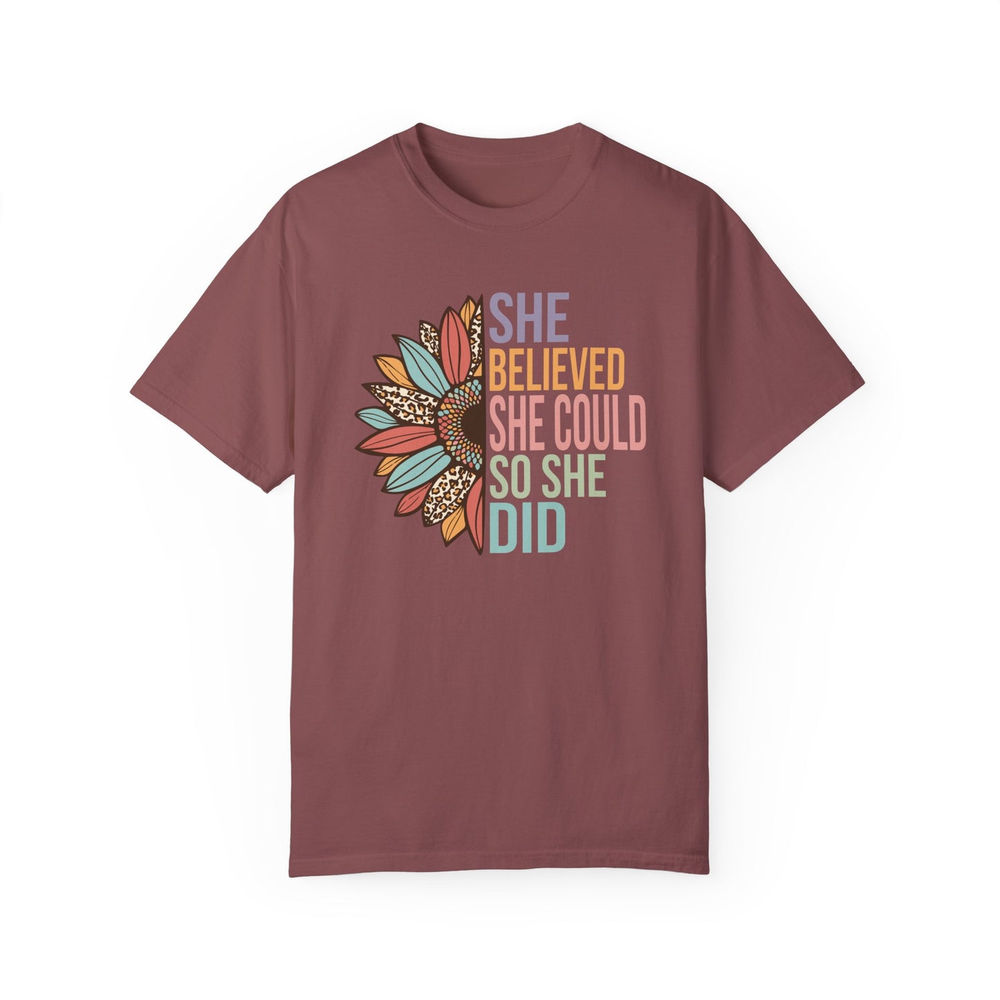 Brick colored t-shirt with the saying "She Believed She Could So She Did" as half of the sunflower and a retro design other half of the flower with petals of leopard print, teal, rust and golden yellow