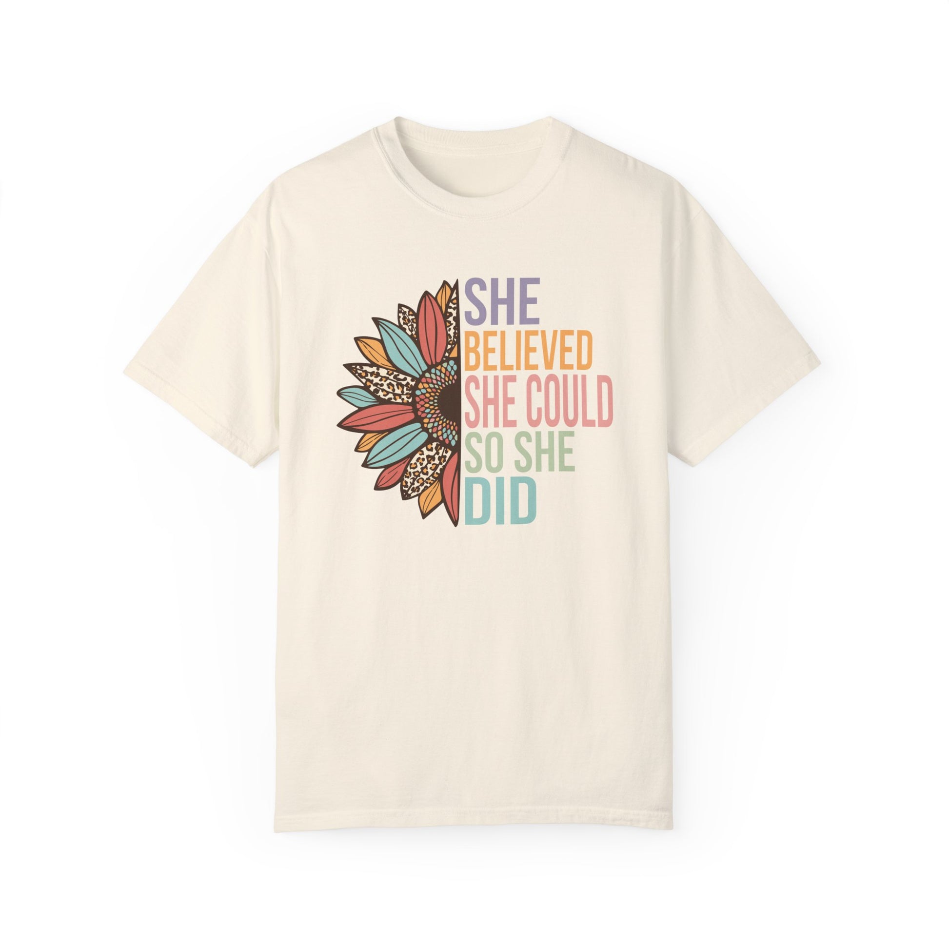 Ivory colored t-shirt with the saying "She Believed She Could So She Did" as half of the sunflower and a retro design other half of the flower with petals of leopard print, teal, rust and golden yellow