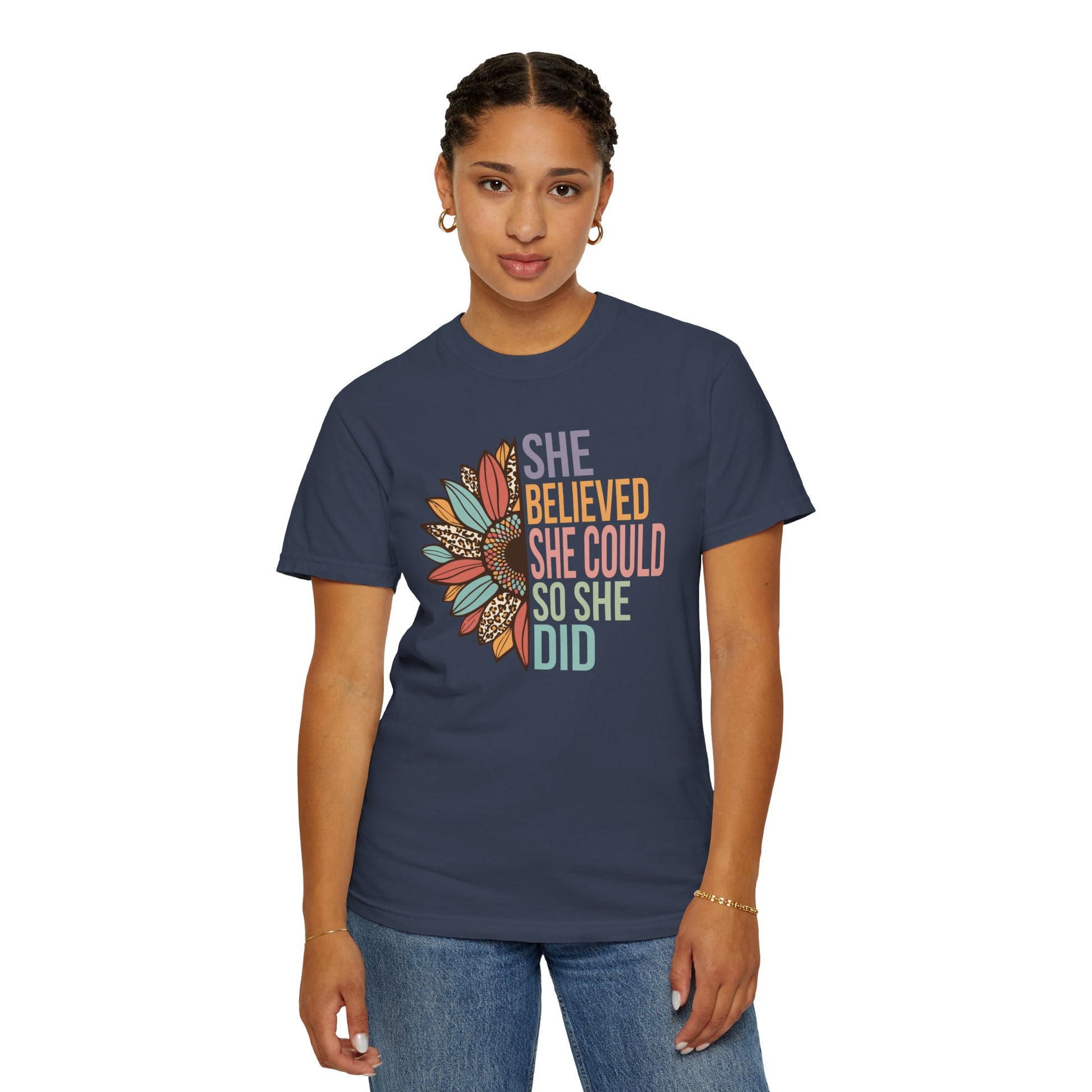 Midnight colored t-shirt with the saying "She Believed She Could So She Did" as half of the sunflower and a retro design other half of the flower with petals of leopard print, teal, rust and golden yellow worn by a woman.