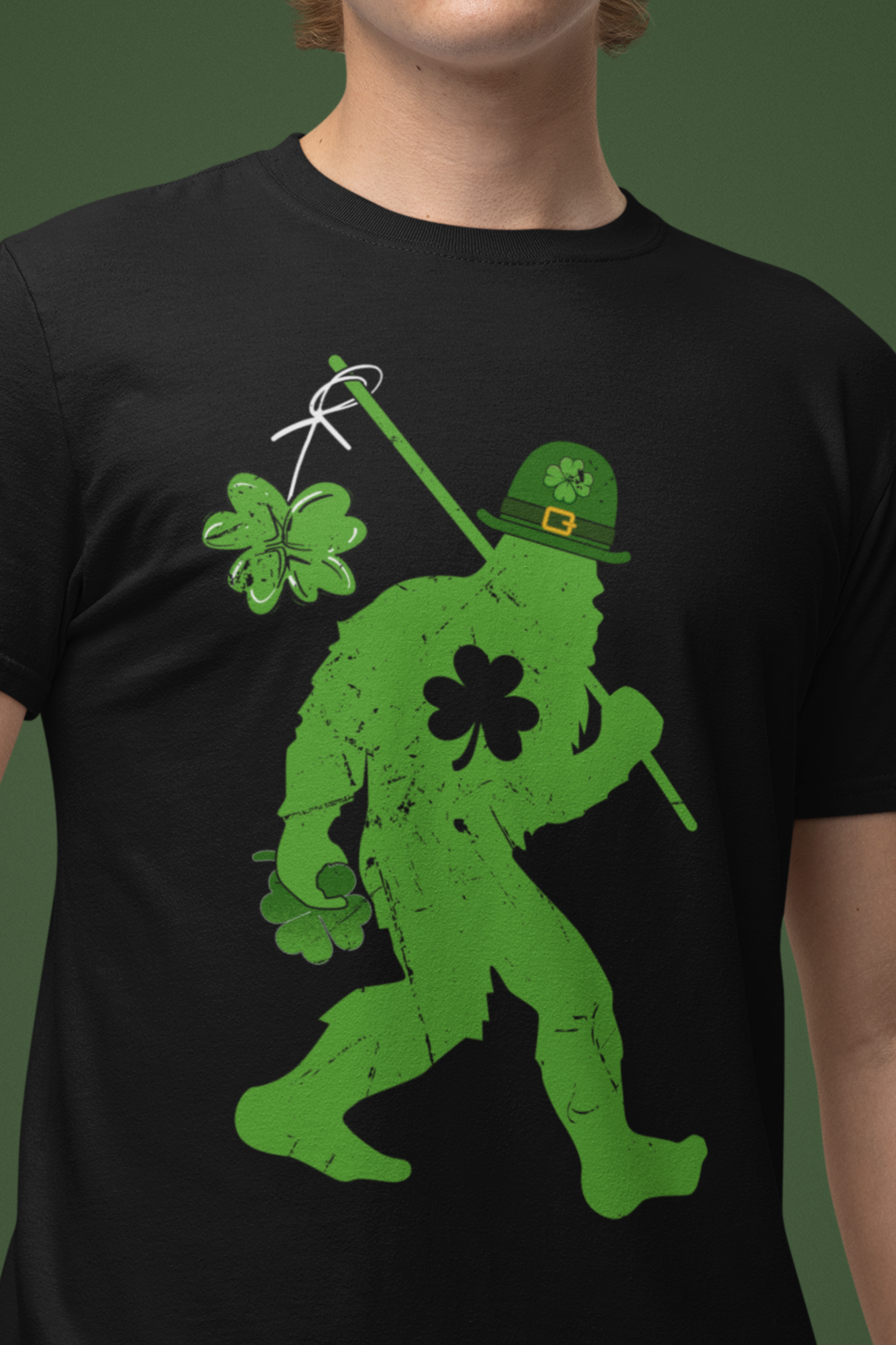 Black color St. Patrick's Day T-shirt with bigfoot wearing a leprechaun hat carrying a fishing pole with a shamrock attached to it. male mock-up