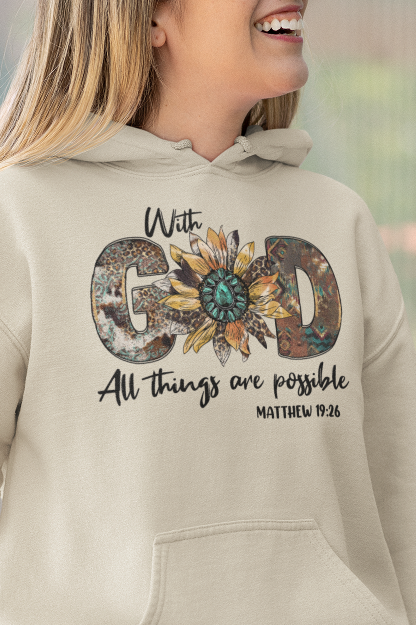 Sand colored hooded sweatshirt with front graphic.  The focus is the word "God" in capitals in a western rustic style with a sunflower representing the O.  The rest of the words are script and it says "With God All Things Are Possible" Matthew 19:26.  Back of hoodie is plain, no graphic.  Modeled by woman.